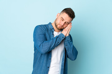 Russian handsome man isolated on blue background making sleep gesture in dorable expression