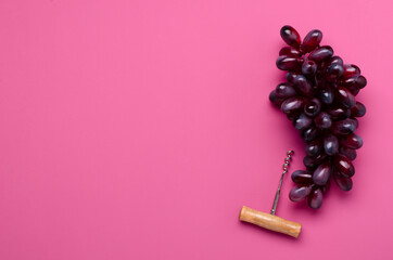 Top view of ripe grapes and handle corkscrew on the empty dark pink background