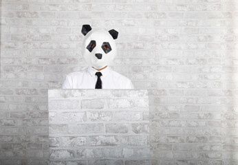 Man with panda mask camouflages himself in a white brick wall