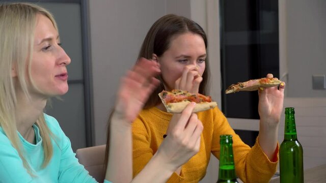 Relax with your friend. Two best happy girlfriends at home in the kitchen eating pizza and drinking beer. They laugh and smile. celebrating.