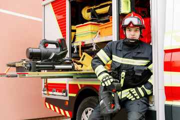 Fototapeta premium A man of strong physique in uniform and helmet stands by a rescue vehicle.