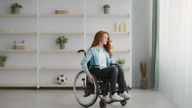 Cute disabled little girl sitting in wheelchair pushing it to window at home, slow motion