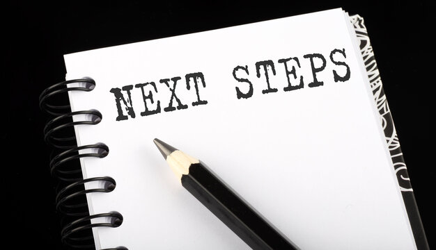 Next Steps Written Text In A Small Notebook On A Black Background