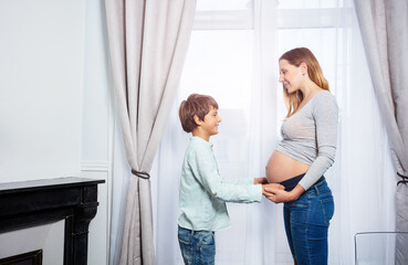 Boy hold pregnant mom belly near the window