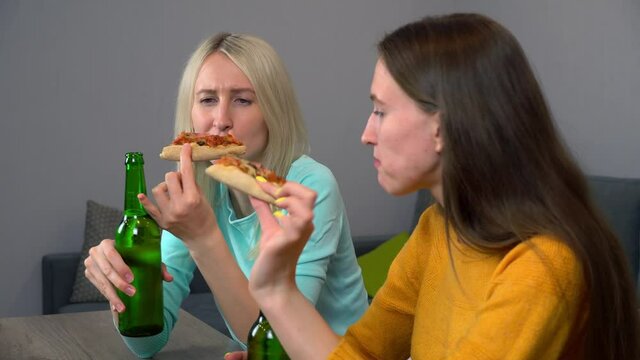 Relax with your friend. Two best happy girlfriends at home in the kitchen eating pizza and drinking beer. They laugh and smile. celebrating.