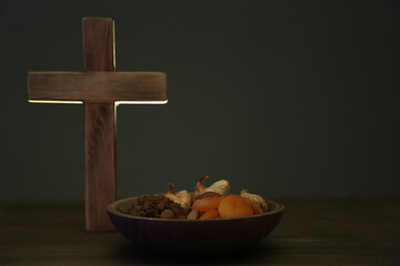 Cross and dried fruits on wooden table, space for text. Lent season