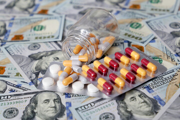 Pills and capsules in a bottle on US dollars bills. Concept of health care in USA, pharmaceutical business, drug prices, pharmacy, medicine and economics