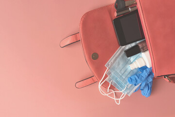 Open womens purse contains rubber gloves, medical masks, antivirus spray, smartphone, lipstick, keys, nail polish on pink background. New normality.Copyspace