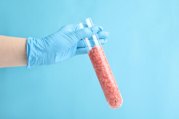 Scientist holding test tube with minced lab grown meat on light blue background, closeup