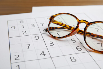 Sudoku and eyeglasses on wooden table, closeup