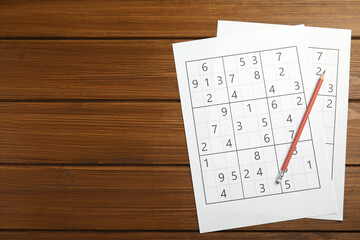 Sudoku and pencil on wooden table, top view. Space for text