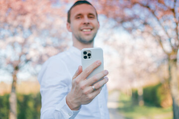 A young man speaks on the phone against the background of a blossoming sakura garden. Spring.