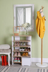 Wooden shelving unit with shoes and different accessories near green wall in hall. Storage idea