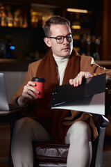 portrait of young businessman working on laptop and with documents in hotel lobby