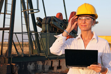 Successful female engineer with a notebook control the operation of the oil pump, close up of smiling young woman with safety goggles looks at sunset