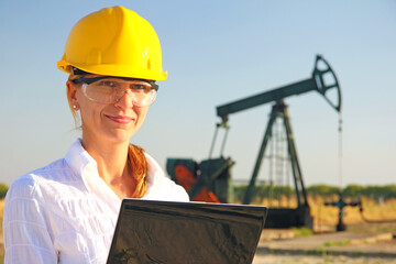 Successful female engineer with a notebook control the operation of the oil pump, close up of smiling young woman with safety goggles