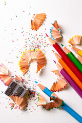Top view of colored pencils with shavings and pencil sharpener over white background. top view.