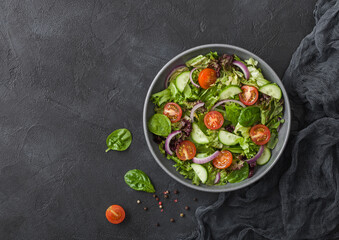 Fresh healthy vegetarian vegetables salad with tomatoes and cucumber, red onion and spinach in grey bowl plate on dark background.