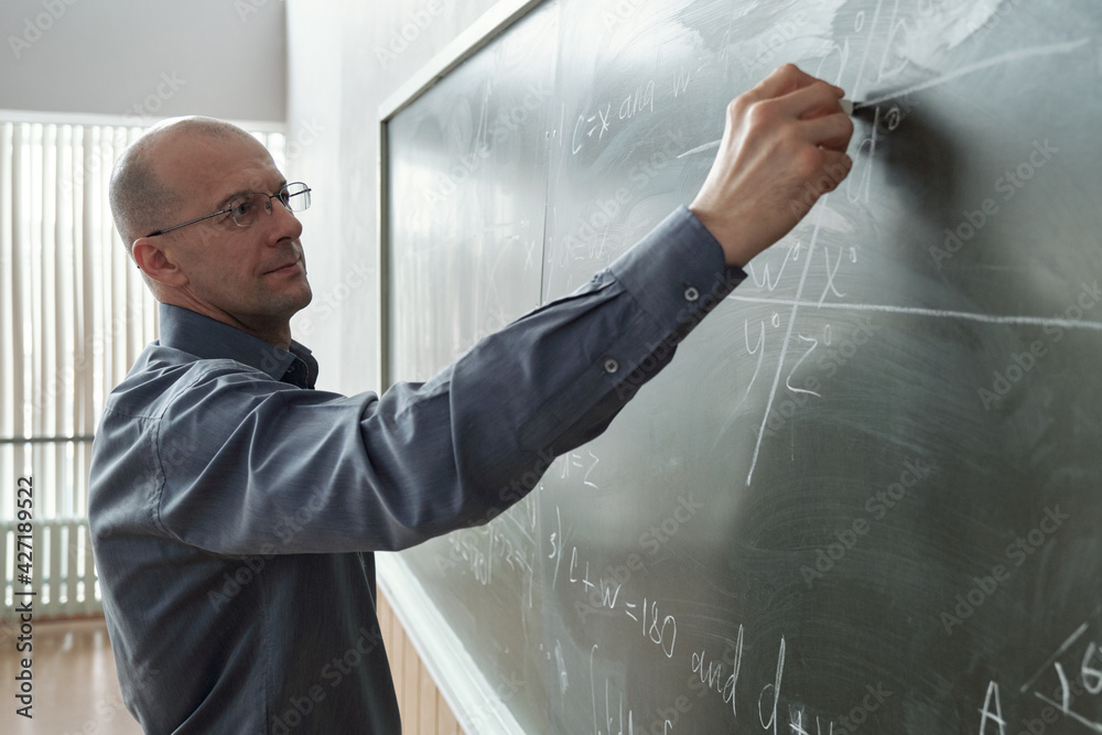 Poster mature professor of university in smart casualwear standing in front of blackboard at lesson in audi