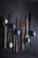 Easter eggs painted with natural blueberry dye lie on wooden spoons on a dark concrete background. dark still life. flat lay.