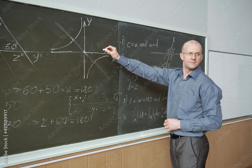 Poster Confident mature professor standing in front of blackboard in lecture hall, pointing at graph and explaining it while looking at audience