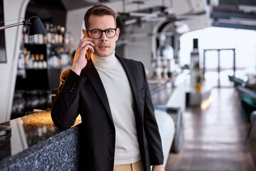 Portrait Of Serious Calm Man In Suit Talking On Phone While Standing In Restaurant