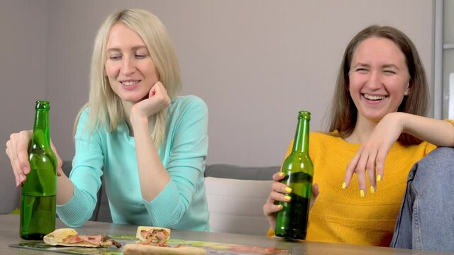 Relax with your friend. Two best happy girlfriends at home in the kitchen eating pizza and drinking beer. They laugh and smile. celebrating.