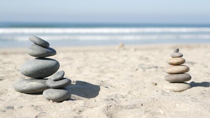 Rock balancing on ocean beach, stones stacking by sea water waves. Pyramid of pebbles on sandy shore. Stable pile or heap in soft focus with bokeh, close up. Zen balance, minimalism, harmony and peace