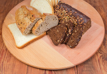 Partly sliced various bread on round wooden cutting board