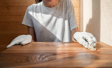 A young girl in work gloves is covering a wooden tabletop with oil. Wood impregnation