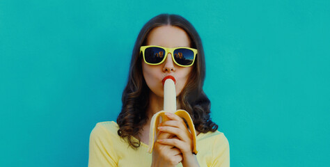 Portrait close up of young woman eating banana on a blue background
