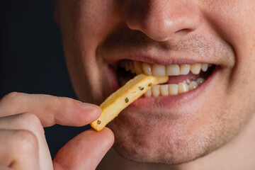 Young man bites fries. Extreme close up. Guy eats eating fried potatoes, isolated. Male mouth.