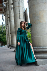 Naklejka premium young elegant woman relaxing and posing for camera near columns in green dress