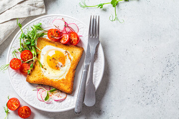 Fried egg in bread toast with tomatoes, radishes and sprouts on white plate, gray background, top view. Healthy breakfast concept.