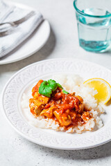 Fried chicken in tomato sauce with rice on white plate, gray background.