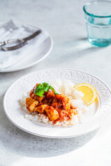 Fried chicken in tomato sauce with rice on white plate, gray background.