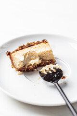 Bitten piece of vegan tofu cheesecake on white saucer. Healthy plant based dessert concept.