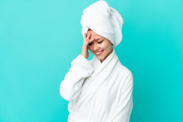 Teenager blonde girl in a bathrobe over isolated blue background laughing