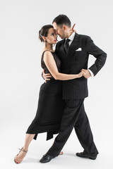 Couple of professional tango dancers in elegant suit and dress pose in a dance move. Attractive man and woman dance looking eye to eye with love and passion on white background.
