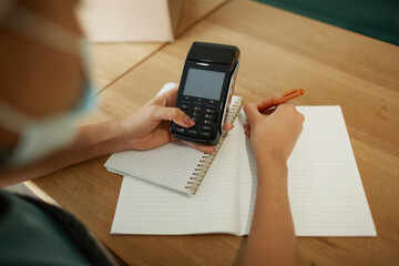 High angle closeup of young African-American woman calculating finances and doing inventory at small business shop, copy space