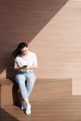 Pretty smiling young woman sitting outdoors on windy day, texting friends and checking posts on social media