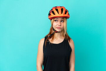 Young cyclist girl over isolated blue background making doubts gesture looking side