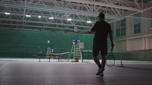 professional male tennis player with ball and racquet on indoor court, rear view, sportsman is dressed sportswear