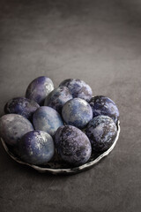 organic Easter eggs close-up, hand-painted with natural blueberries, lie in a clay cup on a stone table. Easter concept.