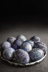 organic Easter eggs on a dark background, hand-painted with natural blueberries, lie in a clay cup on a stone table. Easter concept.