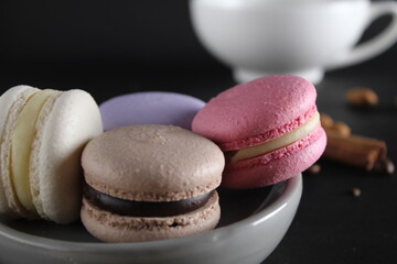 Macaroons on a gray plate at the back stands a cup of coffee or tea coffee beans and cinnamon sticks on a black background with a place for text and with a copyspace