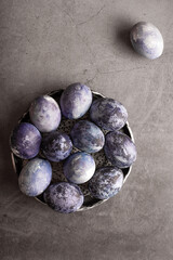 marble Easter eggs on a dark background, hand-painted with natural blueberries, lie in a clay cup on a stone table. Easter preparation concept.