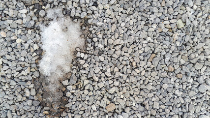 Melting snow on gravel road. Small gravel texture pattern. Rock ground