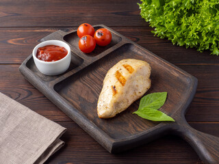 Grilled chicken breast steak with cherry and red sauce on a wooden board. Serve chicken steak in the restaurant.  Juicy fried delicious chicken. Space for text. Rustic style. Copy space.