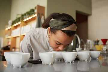 Portrait of mixed race young woman smelling cofeee during quality assesment and cupping test in...